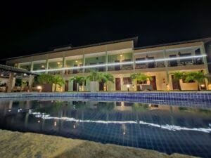 Piscina da Pousada Bellissima Italia à noite com reflexo do prédio iluminado na água.