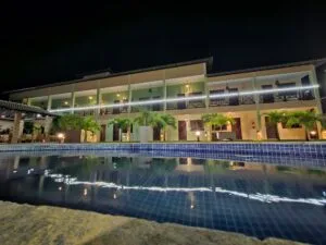 Piscina da Pousada Bellissima Italia à noite com reflexo do prédio iluminado na água.