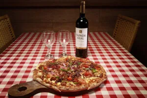 Combinação de pizza e vinho na mesa da Pizzaria Bellissima Italia, Praia de Barro Preto.